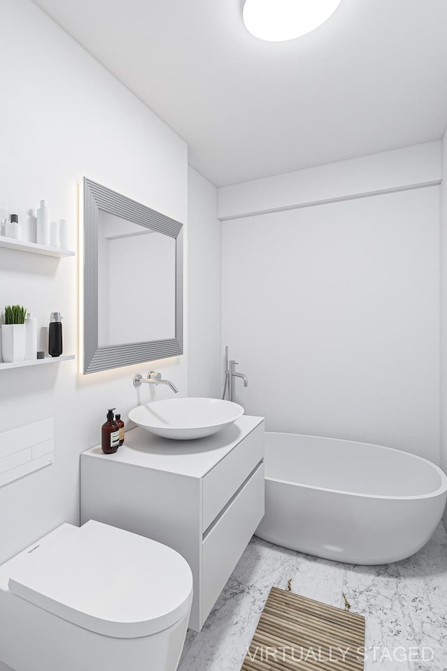 bathroom featuring double vanity, marble finish floor, a freestanding tub, toilet, and a sink