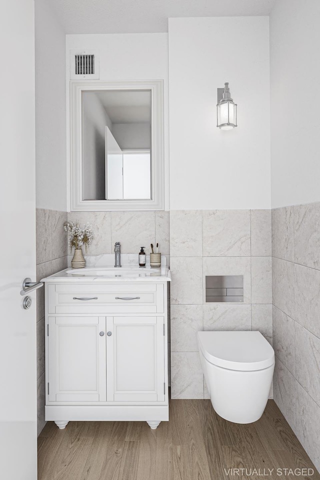 half bath featuring visible vents, toilet, wood finished floors, vanity, and tile walls