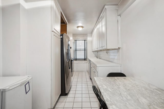 kitchen featuring decorative backsplash, light tile patterned floors, light countertops, freestanding refrigerator, and white cabinetry