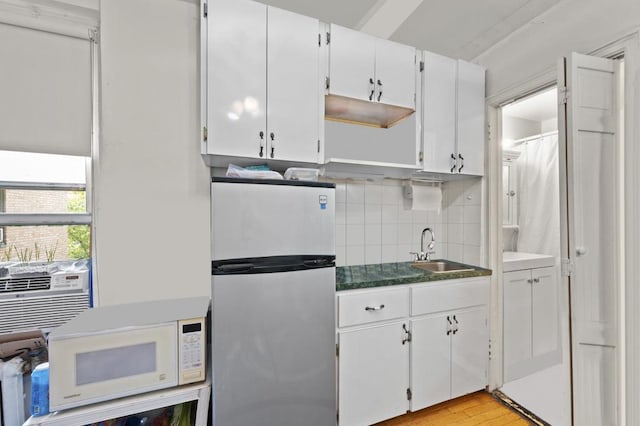 kitchen featuring dark countertops, white microwave, freestanding refrigerator, white cabinetry, and a sink