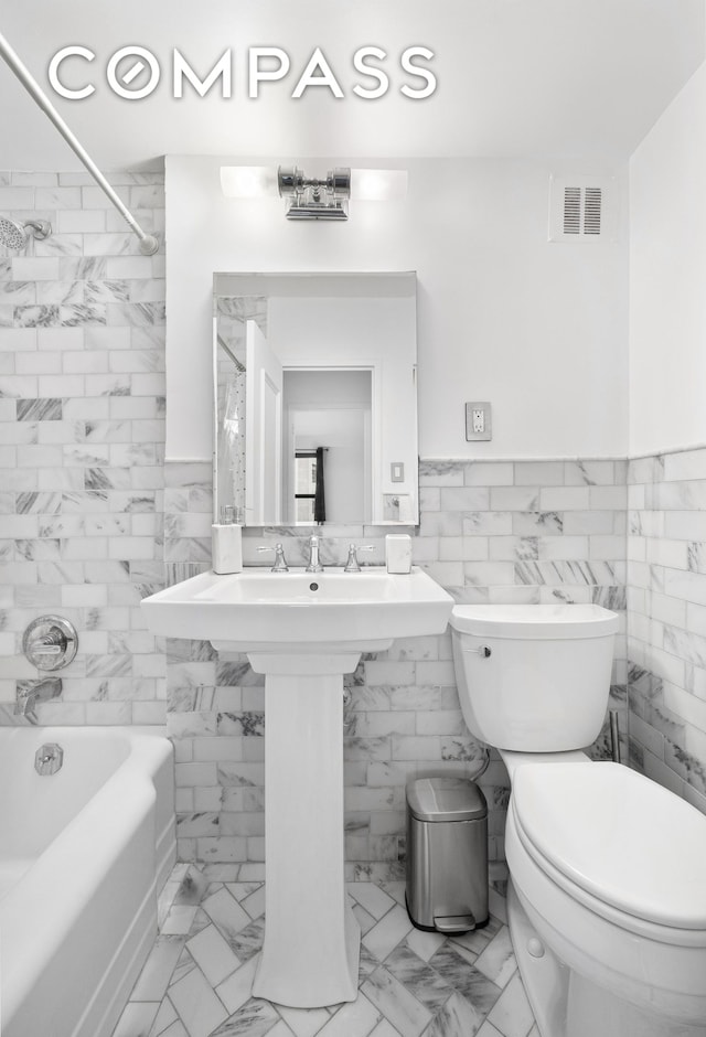 bathroom featuring tile walls, toilet, marble look tile flooring, bathing tub / shower combination, and wainscoting