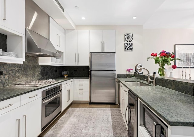 kitchen with appliances with stainless steel finishes, tasteful backsplash, white cabinetry, sink, and wall chimney exhaust hood