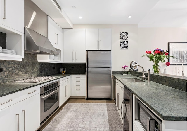 kitchen with stainless steel appliances, tasteful backsplash, a sink, wall chimney range hood, and a peninsula