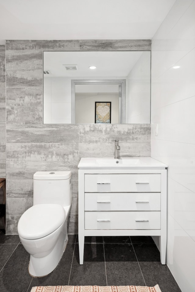 bathroom featuring tile patterned flooring, toilet, vanity, visible vents, and tile walls