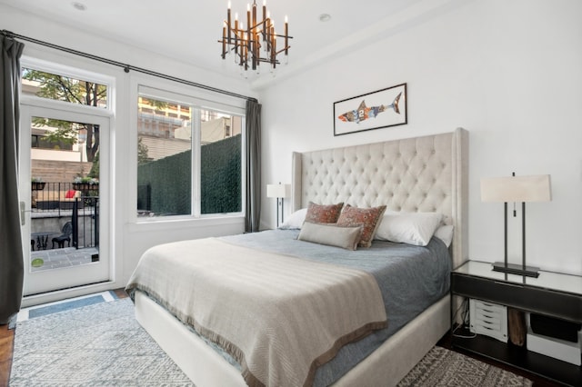 bedroom with access to outside, wood-type flooring, and an inviting chandelier