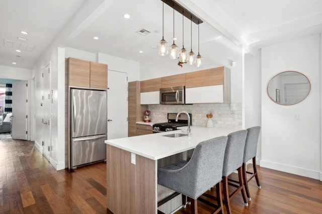 kitchen featuring stainless steel appliances, a peninsula, a sink, a kitchen breakfast bar, and backsplash