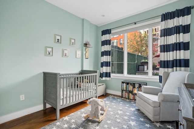 bedroom featuring a crib, baseboards, and wood finished floors