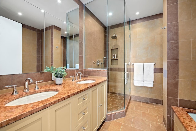 full bath with tile walls, double vanity, a stall shower, and a sink