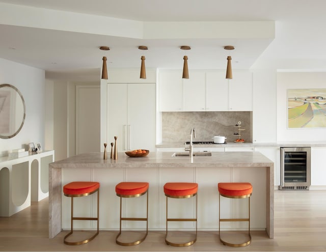kitchen with beverage cooler, a sink, white cabinetry, tasteful backsplash, and a breakfast bar