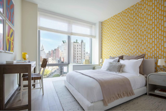 bedroom with wallpapered walls, a city view, an accent wall, and wood finished floors