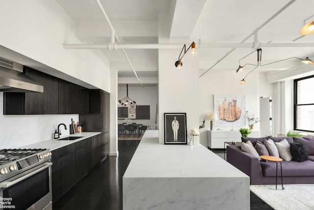 kitchen featuring stainless steel range with gas stovetop, a center island, sink, and wall chimney range hood