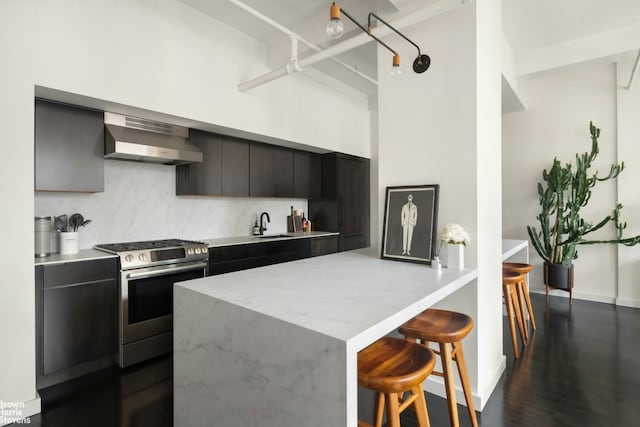 kitchen featuring dark hardwood / wood-style floors, a kitchen breakfast bar, decorative backsplash, wall chimney range hood, and stainless steel gas range