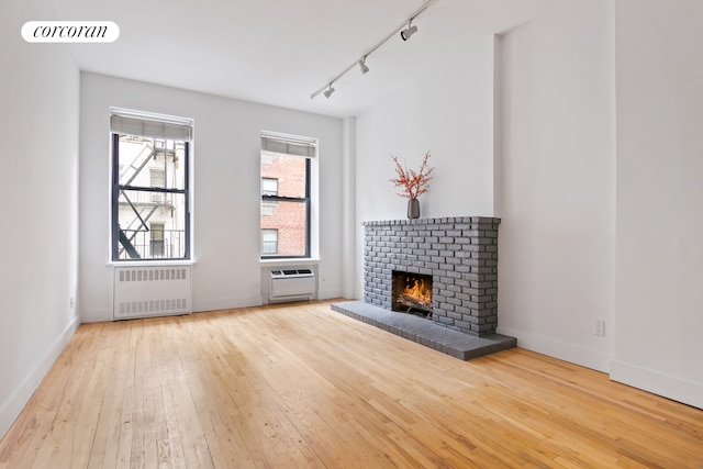 unfurnished living room featuring baseboards, visible vents, radiator, hardwood / wood-style flooring, and a fireplace