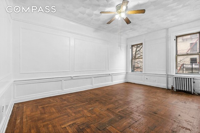 empty room with ceiling fan, dark parquet floors, and radiator heating unit