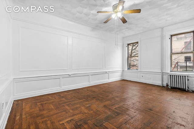 unfurnished room with a decorative wall, radiator, and a ceiling fan