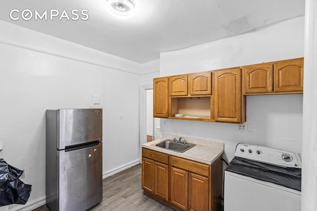 kitchen with wood finished floors, washer / clothes dryer, freestanding refrigerator, a sink, and light countertops