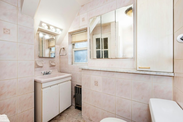 half bathroom with vanity, toilet, radiator, tile walls, and vaulted ceiling