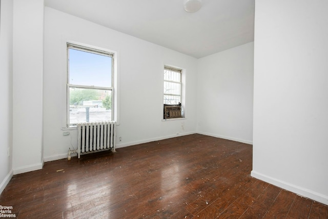 empty room featuring dark wood-type flooring, radiator heating unit, and baseboards