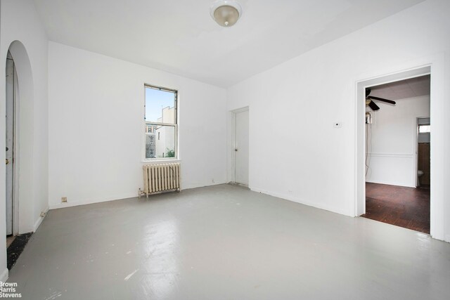 unfurnished room featuring arched walkways, concrete flooring, and radiator heating unit