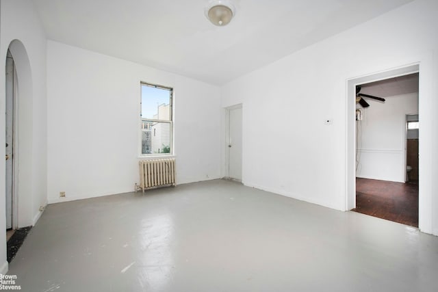 empty room featuring arched walkways, radiator, and concrete floors