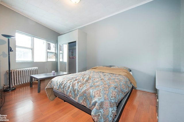 bedroom featuring a closet, radiator, ornamental molding, and wood finished floors