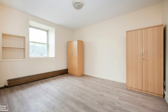 unfurnished room with a baseboard heating unit, light wood-style flooring, and baseboards