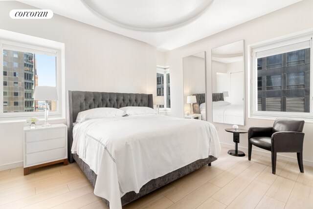 bedroom with light wood-type flooring, a raised ceiling, visible vents, and baseboards