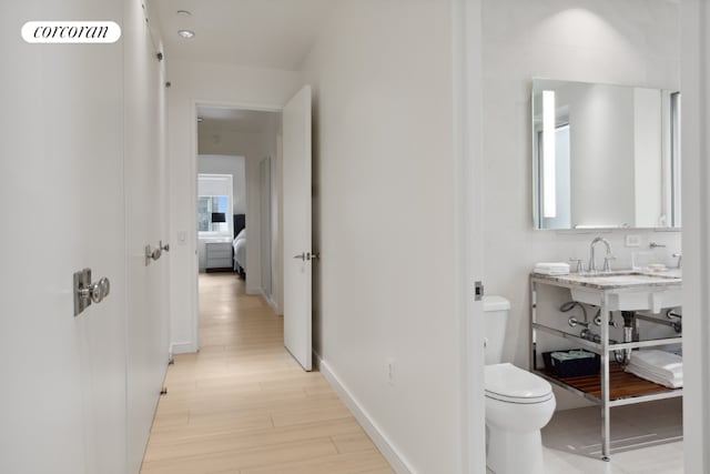 corridor featuring light wood-style floors, baseboards, visible vents, and a sink