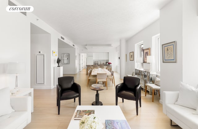 living area with a textured ceiling, light wood finished floors, and visible vents