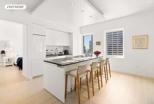 kitchen with dark countertops, visible vents, white cabinetry, light wood-type flooring, and a kitchen breakfast bar