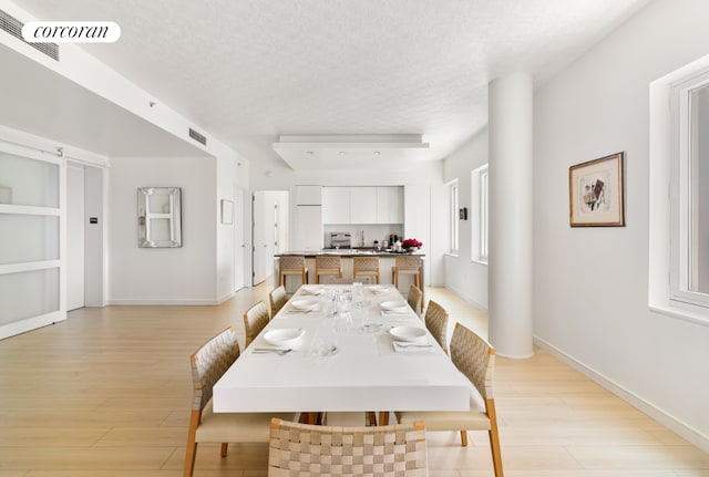 dining room featuring a textured ceiling, light wood finished floors, visible vents, and baseboards