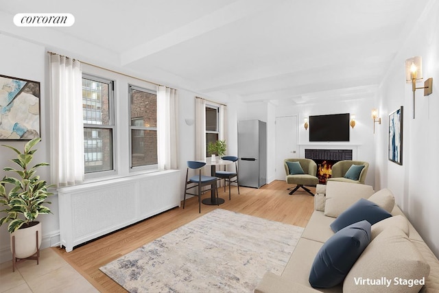 living room featuring a brick fireplace, visible vents, wood finished floors, and beamed ceiling