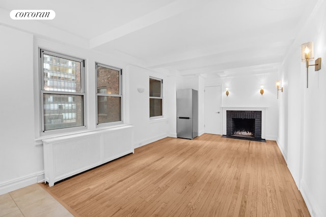 unfurnished living room with beam ceiling, a fireplace, visible vents, radiator heating unit, and light wood-style floors