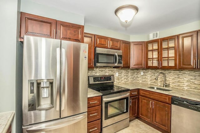 kitchen with appliances with stainless steel finishes, sink, backsplash, light stone counters, and light tile patterned floors