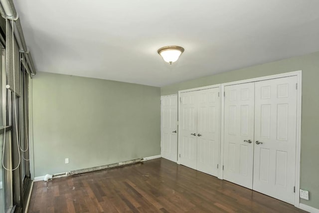 unfurnished bedroom featuring dark wood-type flooring, a baseboard heating unit, and multiple closets