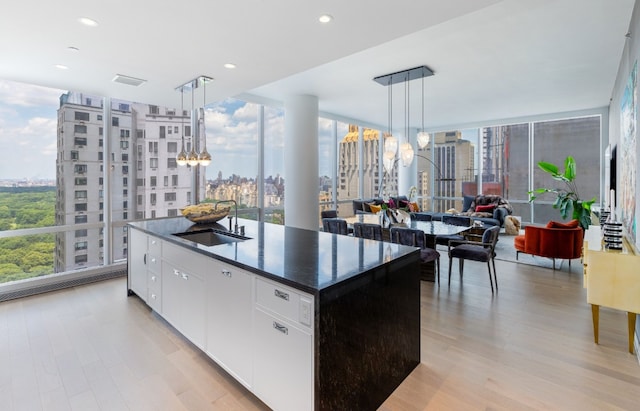 kitchen featuring decorative light fixtures, sink, white cabinets, a wall of windows, and a center island with sink