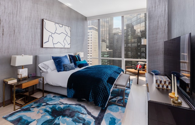 bedroom featuring a view of city, wood finished floors, and floor to ceiling windows