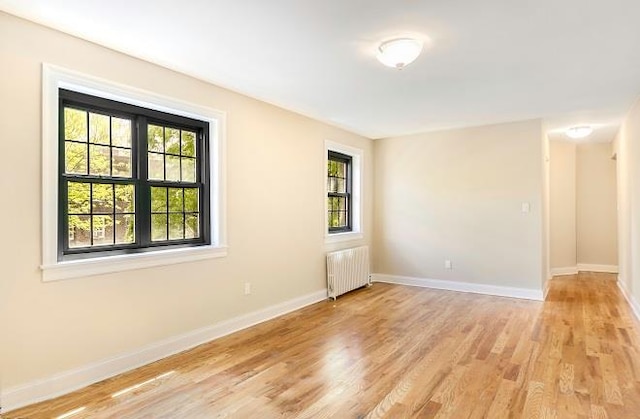 spare room with light wood-style floors, radiator heating unit, and baseboards