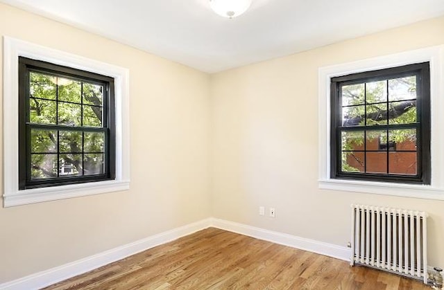 unfurnished room featuring hardwood / wood-style flooring, a healthy amount of sunlight, and radiator heating unit