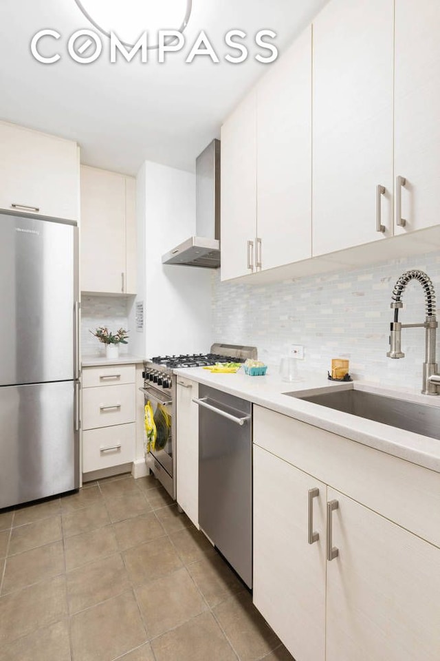 kitchen with wall chimney exhaust hood, appliances with stainless steel finishes, light countertops, white cabinetry, and a sink