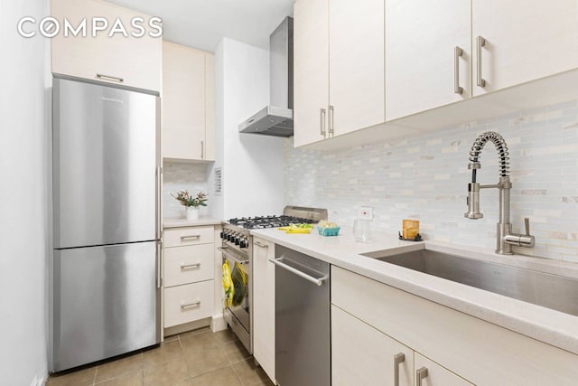 kitchen featuring stainless steel appliances, a sink, light countertops, wall chimney exhaust hood, and tasteful backsplash