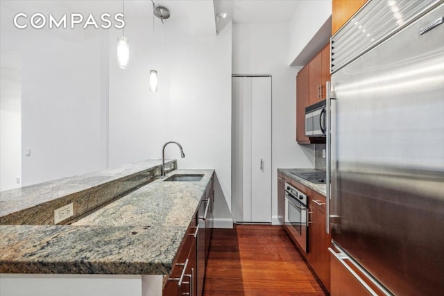 kitchen with stainless steel appliances, sink, stone countertops, dark hardwood / wood-style floors, and pendant lighting