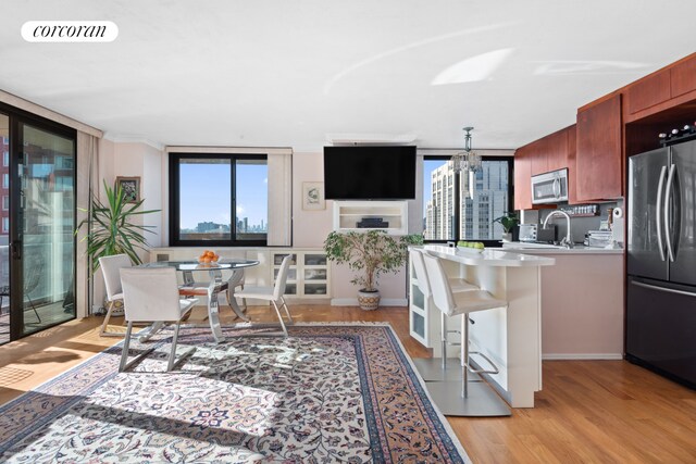 kitchen with sink, appliances with stainless steel finishes, an inviting chandelier, a kitchen breakfast bar, and light wood-type flooring