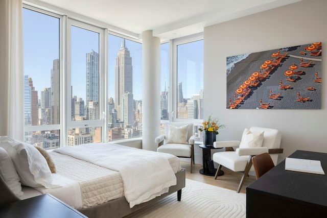 bedroom with floor to ceiling windows, wood finished floors, and a city view