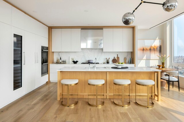 kitchen with light countertops, light wood-style flooring, decorative backsplash, modern cabinets, and a kitchen bar