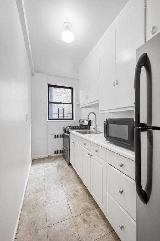 kitchen featuring radiator heating unit, refrigerator, sink, white cabinets, and stainless steel range with gas stovetop