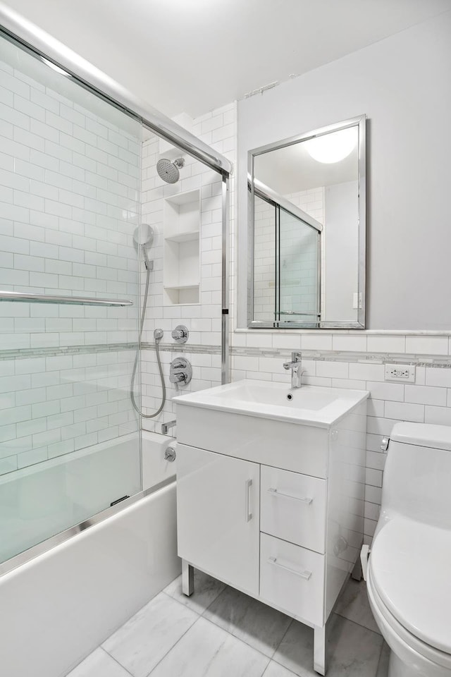 full bathroom featuring toilet, combined bath / shower with glass door, tile walls, and vanity