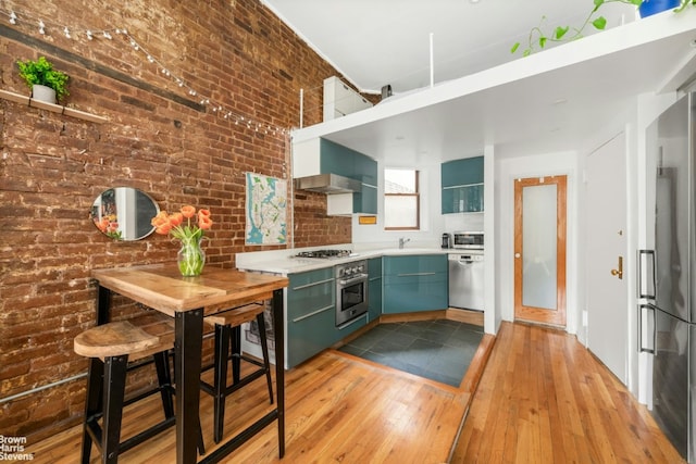 kitchen with brick wall, stainless steel appliances, sink, and light wood-type flooring