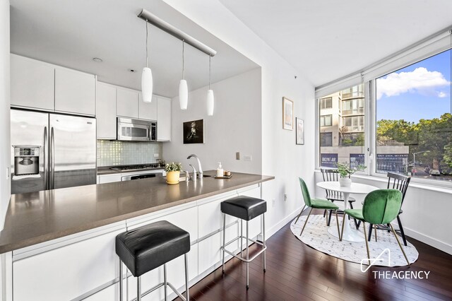 kitchen with tasteful backsplash, white cabinetry, hanging light fixtures, a breakfast bar, and stainless steel appliances