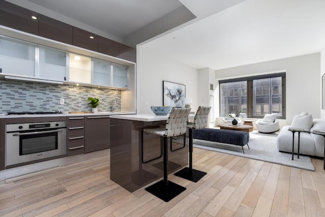 kitchen featuring a breakfast bar area, light countertops, stainless steel oven, modern cabinets, and open floor plan